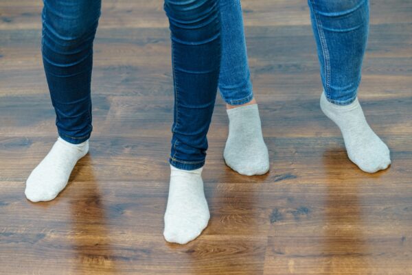 Women feet standing on wooden floor wearing blue jeans and light socks.