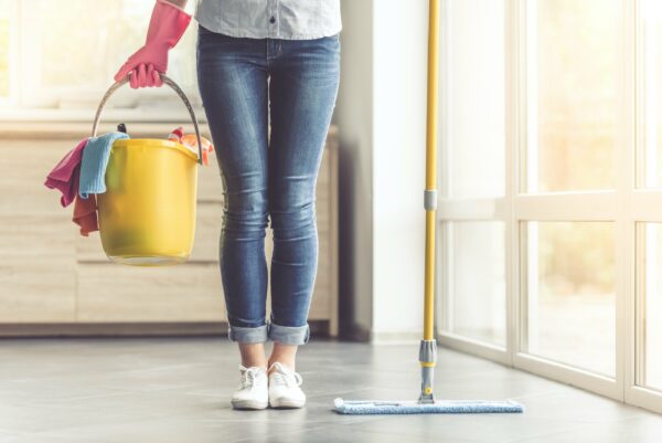 Cropped image of beautiful woman in protective gloves holding a flat wet-mop and bucket with detergents and rags while cleaning her house